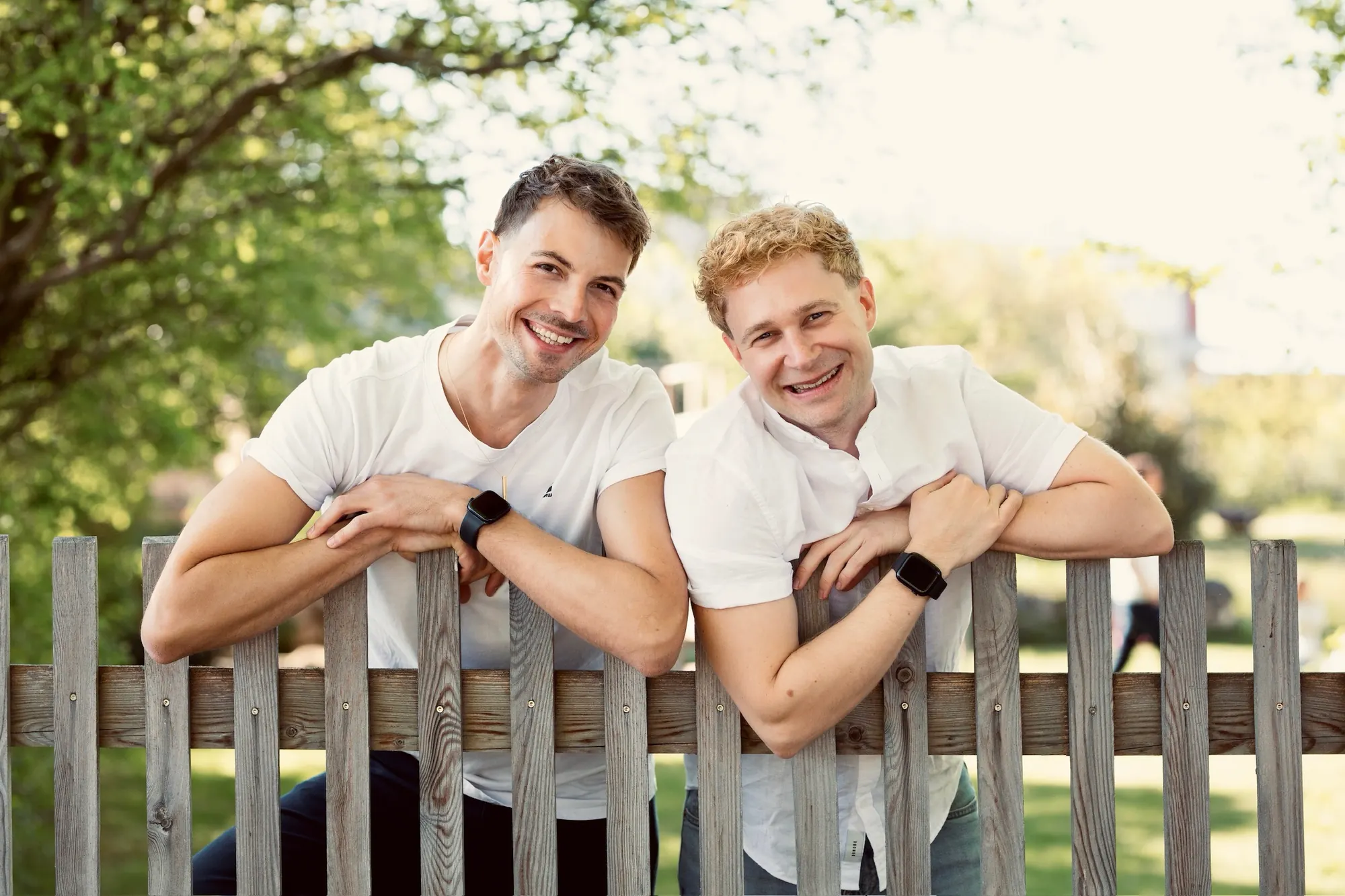 Mathias und Armin lehnen lachend an einem Holzzaun